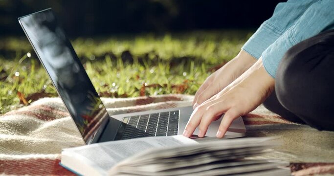 Close up of young woman in casual wear sitting on soft plaid at park and typing on wireless laptop. Female student studying on computer on fresh air.