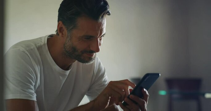 Authentic close up shot of an young man is sitting on a bed and using a smart phone for send messages, make calls or navigate in internet just waked in bedroom at home.