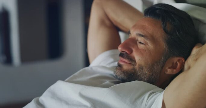 An young handsome man is relaxing and enjoying rest by leaning on soft comfortable bed in a bedroom at home. - Powered by Adobe