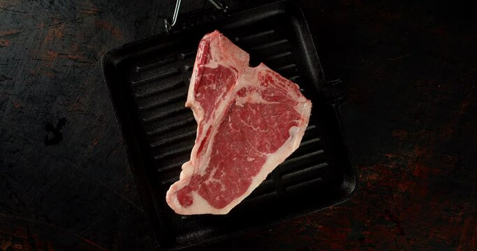 Steak t-bone raw beef in a frying pan slowly rotates. 