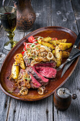 Traditional barbecue wagyu rib eye beef steak very rare and sliced with fried onions and potatoes offered as closeup on a rustic design plate