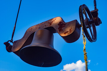 Decorative bell on a blue sky background. A bell with a frayed rope. Mechanism for actuating the...