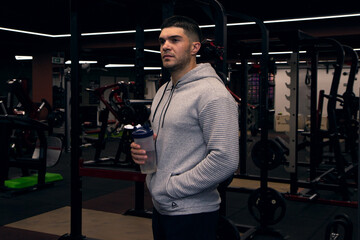 Fototapeta na wymiar Muscular men drinks protein or water, energy drink in the gym. Sportsman holding shaker