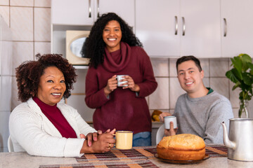 Portrait of latin interracial couplewith mother in law relaxing and enjoying in kitchen home, indoors. Relationship, leisure, enjoyment, aging concept..