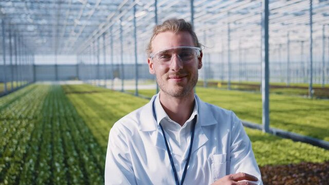 Caucasian young greenhouse worker in protective clothing standing inside modern hothouse. Portrait of successful farm engineer. Eco food. Farming business. Organics.