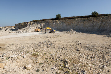 A large yellow tracked excavator is mining rock in a quarry.