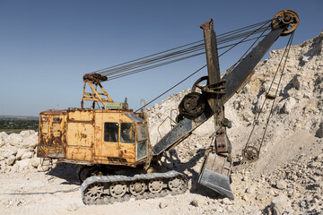 A large yellow tracked excavator is mining rock in a quarry.