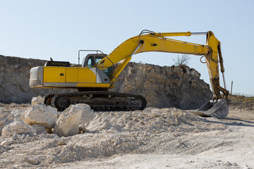 Obraz premium A large yellow tracked excavator is mining rock in a quarry.
