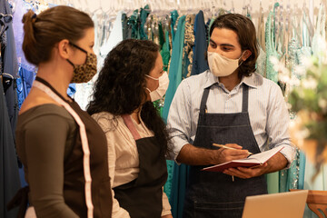 Professional brazilian business team with face mask discussing sales strategy and planning inside shop. owner, small business, successful, community concept..