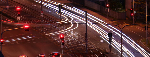 Tram lines, traffic signs, traffic lights and car light trails at a road intersection at night © Simon