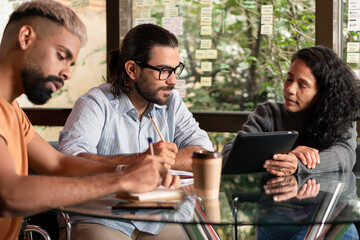 Professional brazilian teammates with tablet collaborating and discussing project plans inside coworking office. Unity, teamwork, collaboration concept..