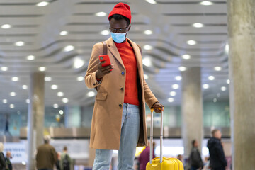 African American traveler man with yellow suitcase stands in airport terminal, using phone, calling...