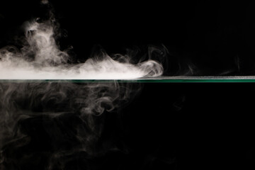 White smoke swirling spreads over the surface flowing down from the edges on a black background