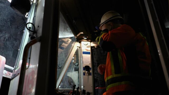 A worker in a mine wearing a hard hat and earplugs operates a drilling machine.