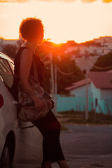 Obraz na płótnie Canvas Mulher admirando o por do sol na cidade, apoiada em um carro branco