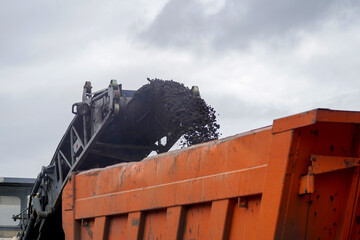 From the conveyor of a road milling machine, cut black asphalt is poured into an orange truck body. © Борис Бондарчук