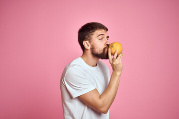Young man with orange on a pink background in a white t-shirt emotions fun gesticulating with model...