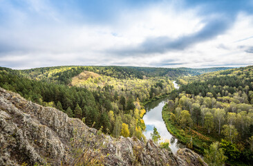 Fototapeta na wymiar Top view of the winding river among the mountains and forests under the cloudy sky in autumn in Siberia, Russia