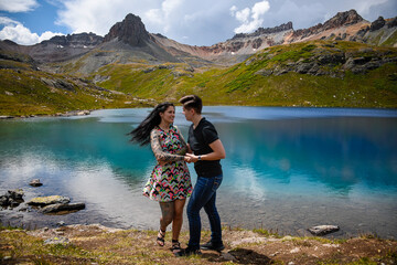 Lesbian couple dancing at a lake with glossy blue water and mountains in the background