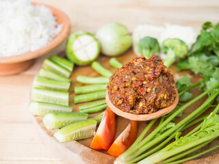 Fermented fish spicy dip with fresh vegetables cucumber, long beans, Broccoli, coriander, tomato, eggplant on wooden background. Thai traditional food.