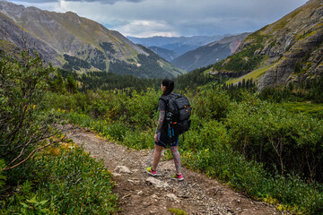 Female hiker walking on a path in the mountains with a forest and clouds