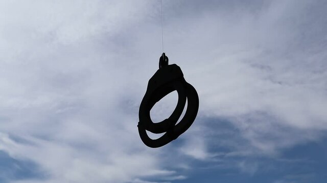 Rusty police handcuffs moving isolated on blue sky and white cloud background closeup.