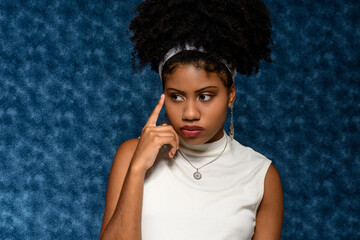 Black Afro-Brazilian teenager with his finger close to his pensive face , on a blue background 