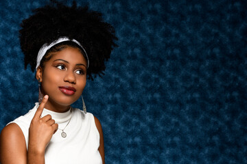 young woman looks to the side with thoughtful expression, afro style woman isolated on blue background, space for text, advertising concept