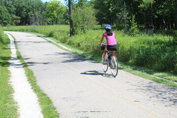 Woman in a pink shirt riding a bicycle on the North Branch Trail at Miami Woods in Morton Grove, Illinois