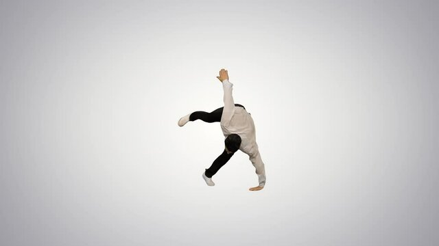 Young man dressed in white shirt and black pants dancing break-dance and smiling at camera at the end on gradient background.
