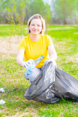 Smiling woman scavenges garbage in the summer park. Volunteer and ecology concept