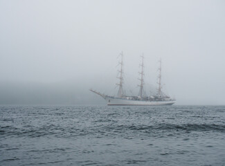 Fototapeta na wymiar A large white sailboat floats on the sea through the strait in the fog.