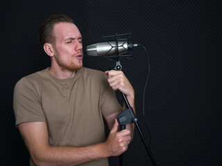 Young caucasian man singing in front of black soundproofing walls. Musicians producing music in professional recording studio.