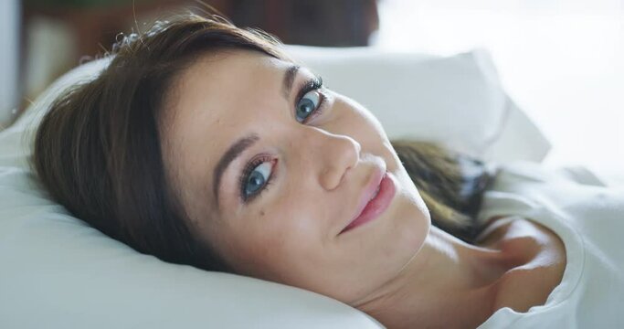 Authentic close up shot of healthy happy woman is smiling in camera just woke up with a sun beams in her bedroom in a morning. Concept: wellbeing, healthcare, lifestyle, bedding, happiness, femininity