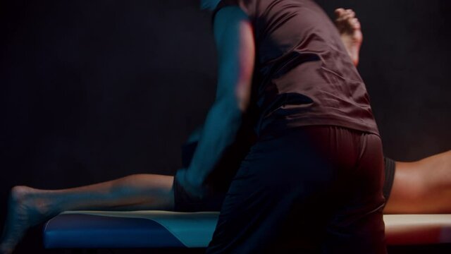 Chiropractic therapy in the dark studio - a therapist working with his client's leg with an effort