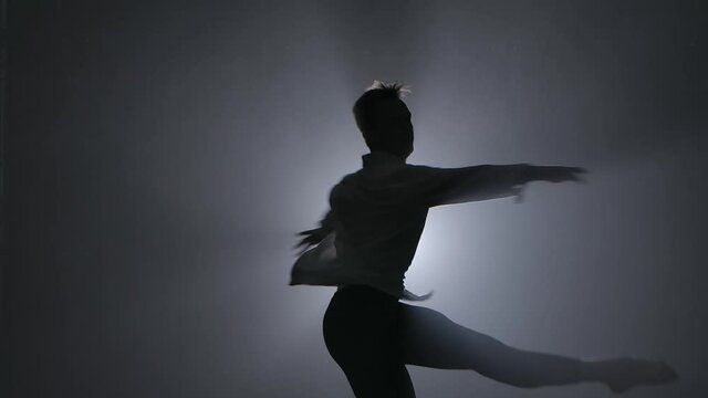 A pirouette performed by a male ballet dancer performing in a dark smoky studio. Silhouettes in the spotlight. Close up in slow motion.