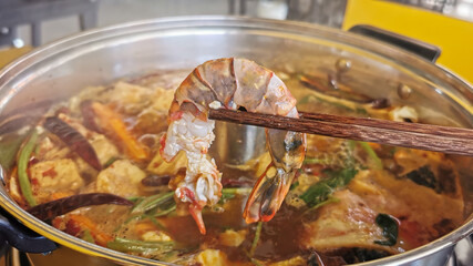 Cooked Tiger prawn in hot boil spicy soup with vegetable beef raw meat or sea food hold with chopsticks.