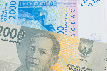 A macro image of a grey two thousand Indonesian rupiah bank note paired up with a blue, two thousand West African franc bank note.  Shot close up in macro.