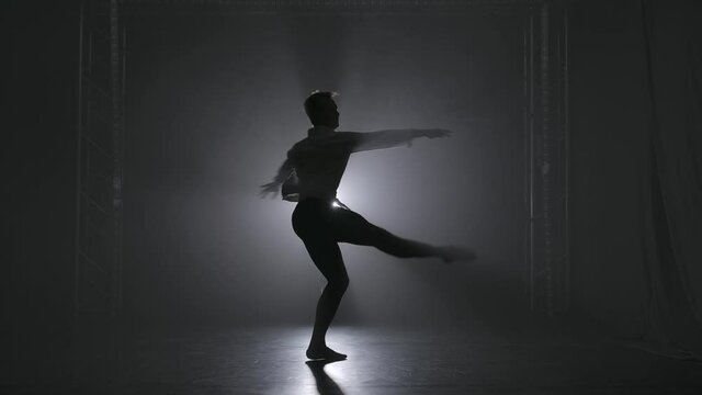 A pirouette performed by a young talented male ballet dancer. Silhouette in the spotlight on a smoky background. Slow motion.