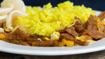 Nasi kuning or yellow rice, traditional food from Indonesia, for breakfast, combine wiith egg, tempeh, and crackers or kerupuk