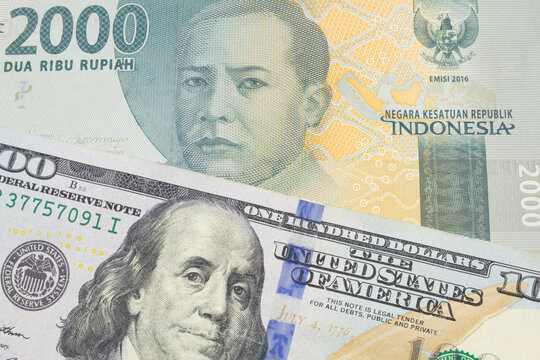 A macro image of a grey two thousand Indonesian rupiah bank note paired up with a blue, one hundred dollar bill from the United States.  Shot close up in macro.
