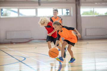 Kids in bright sportswear playing basketball in the gym