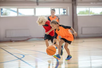 Fotobehang Kids in bright sportswear playing basketball in the gym © zinkevych