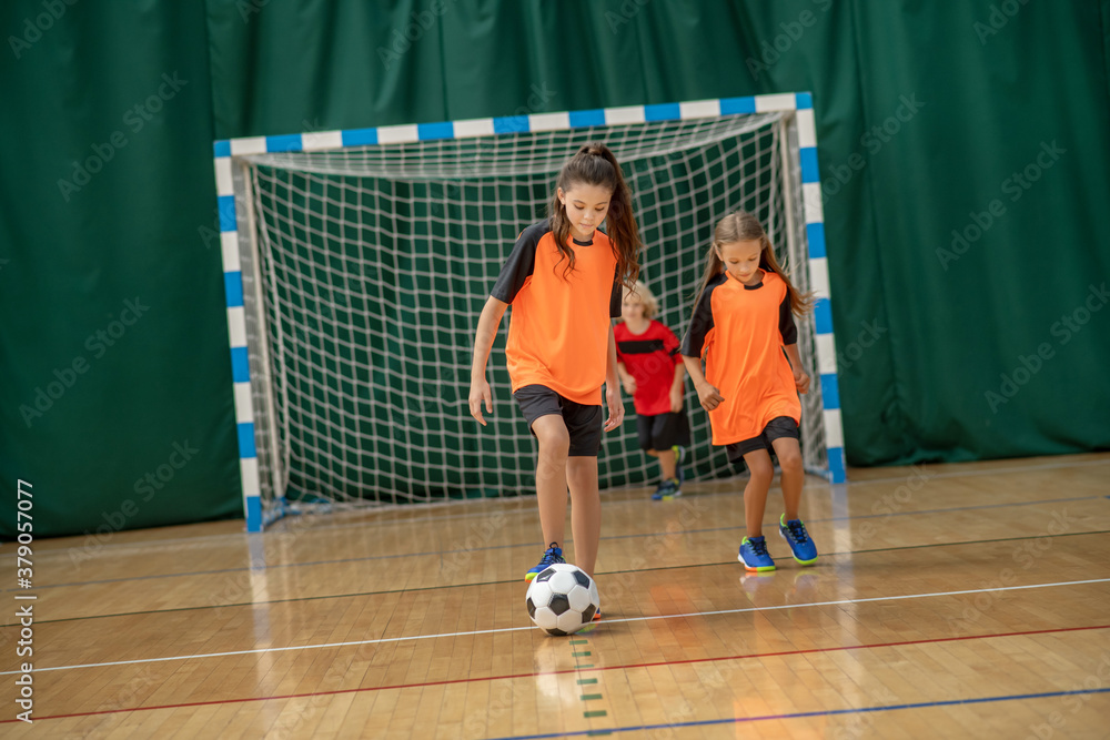 Wall mural Kids in sportswear playing indoors football in the gym