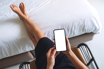 Top view mockup image of a woman holding mobile phone with blank white desktop screen while relaxing and lying on the bed