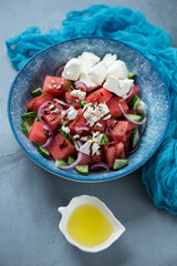 Blue plate with watermelon, feta cheese and cucumber salad, studio shot on a grey concrete background