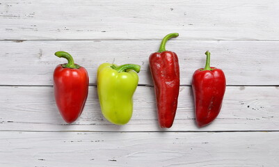 top view of  three red and one yellow peppers arranged in a row on old rustic white wooden table, copy space