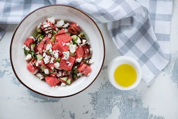 Bowl of watermelon, feta cheese and cucumber salad on a white concrete background, above view, horizontal shot