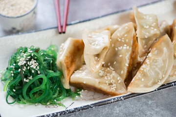 Closeup of pan fried gyoza dumplings served with seaweed salad and sesame seeds, selective focus