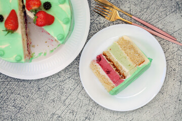 A piece of layered cake with berries and pistachio on a plate. Top View